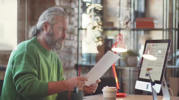 Senior Businessman Using Computer and Taking Notes in Office