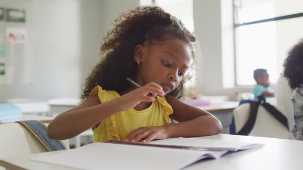 Video of focused african american girl sitting at desk during lesson in classroom