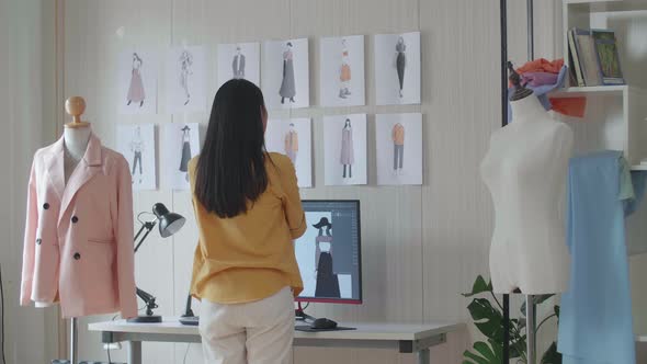 Female Designer Walking To Look At The Pictures On The Wall While Designing Clothes In The Studio