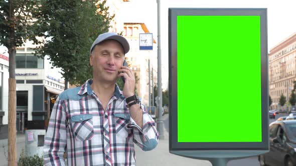 A Middle-aged Man Is Standing on a City Street Next To a Billboard