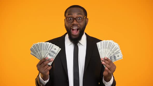 Smiling African-American Businessman Showing Bunches of Dollar Cash, Profit