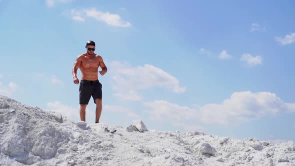 Muscular man walking on white canyon. Strong shirtless man in black glasses going down
