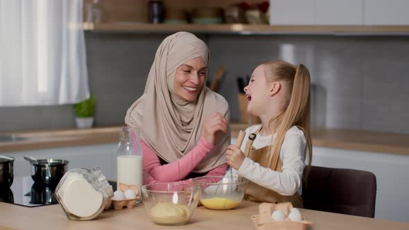 Adorable Little Girl Whisking Eggs in Bowl for Breakfast and Laughing Loving Muslim Mother Watching