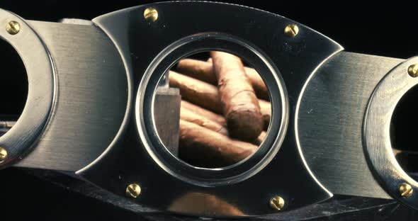 View through a cigar cutter. Cigars in humidor with lighter