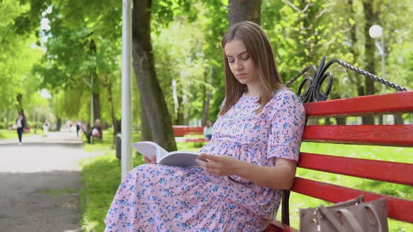 Pregnant Woman in a Summer Dress with a Floral Print Walks in the Park