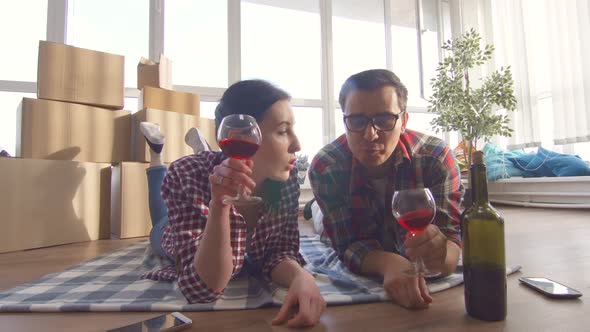 Young Couple Lies on the Floor Drinking Wine and Notes Moving Into a New Apartment