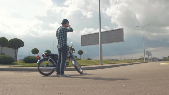 Young Stylish Motorcyclist Goes to His Custom Motorcycle on Street Road at Sunset Slow Motion