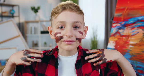 Boy with Hands in Paints Drawing Lines on His Face in Home art studio