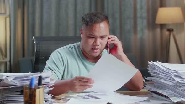 Close Up Of Fat Asian Man Talking On Phone While Working Hard With Documents At Office