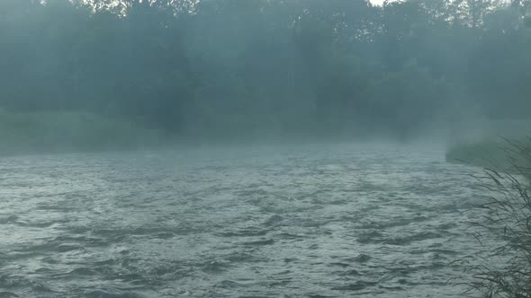 Relaxing running river waters with steam rising across the treeline. Static.