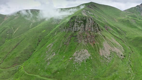 Drone Flight Near Mountain Rock Among Sloping Green Meadows