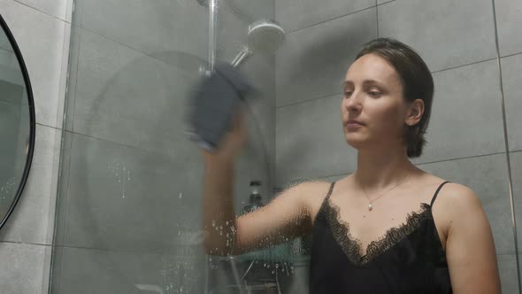 Woman wiping shower glass door with rag. Female cleaning and washing dirty bathtub