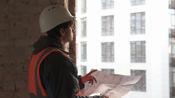 A civil engineer is working with blueprints at the construction site of a high-rise building.