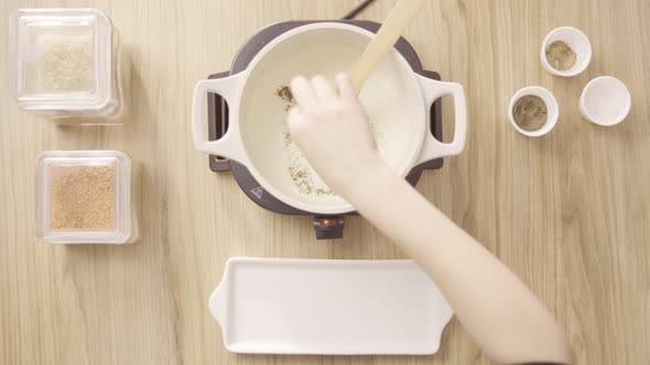 Female chef pouring salt and spices to white soup and use spatula, top shot static