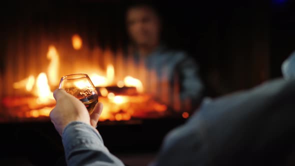 A Man Drinks Brandy By the Fireplace, His Face Is Reflected in the Glass of the Furnace