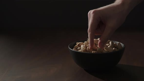 Slow Motion Man Take Roasted Pistachios From Black Bowl on Walnut Table