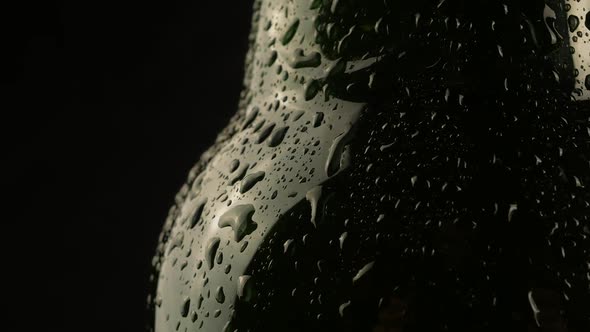 Drop of condensation drips on beer bottle glass. Water drops falling down