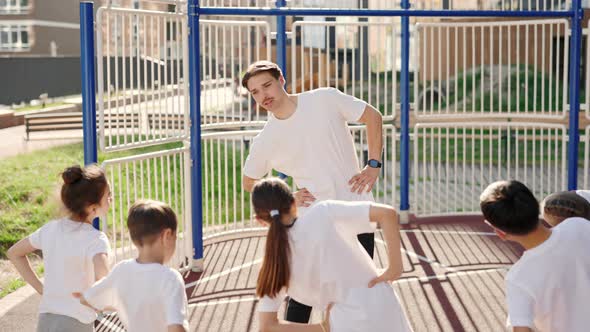 Male Coach and Primary School Children Do Warm Up Before the Workout Outdoor