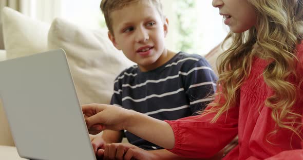 Siblings using laptop in living room