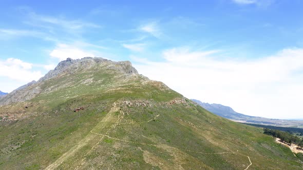 Aerial drone rotating around green mountain peak with forest and mountain range in background, summe