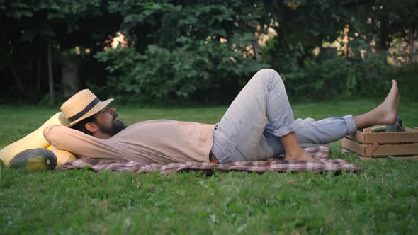 Side View of Young Male Farmer Sleeping Lying on Green Meadow with Harvest