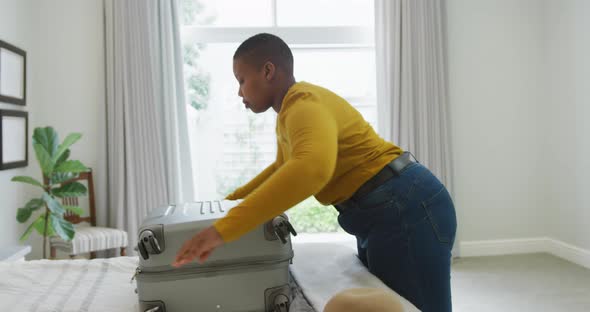 Happy african american plus size woman packing suitcase in bedroom