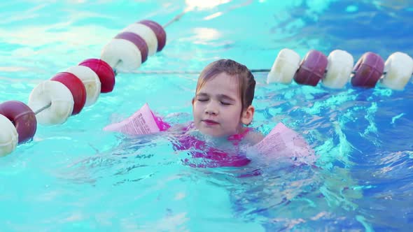 a Funny Little Girl Swims in Inflatable Armbands in a Pool Near the Buoys