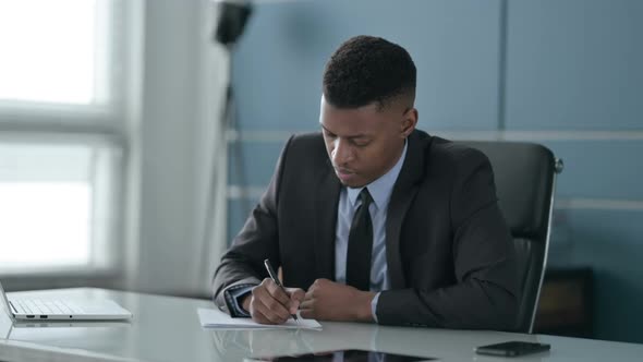 African Businessman Writing on Paper in Office