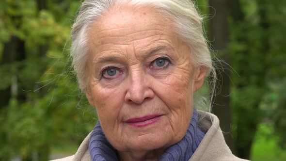 An Elderly Woman Looks Seriously at the Camera in a Park - Face Closeup