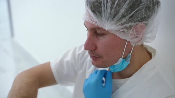 Closeup Frustrated Doctor Taking Off Covid19 Face Mask Sighing Leaning on Wall Sitting on Floor