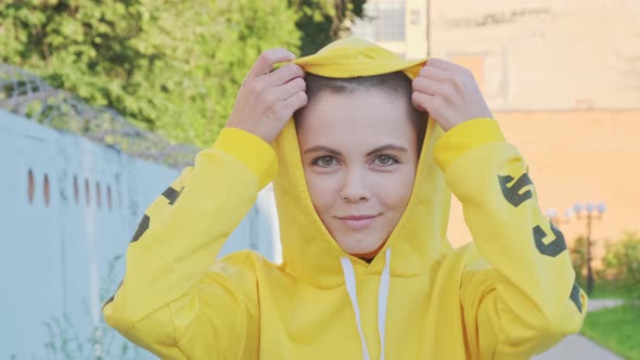 Close Up of Young Smiling Woman in Yellow Hoodie with Shaved Hair in Urban Outdoor City Background. 