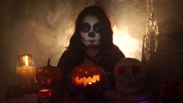 Girl in Skull Makeup Holds a Pumpkin a Lantern with Candles in Hands and Stretches It Forward