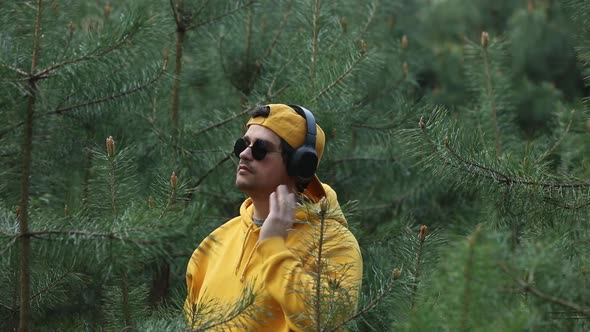 Stylish girl in hoodie listen music in headphones in pine tree forest