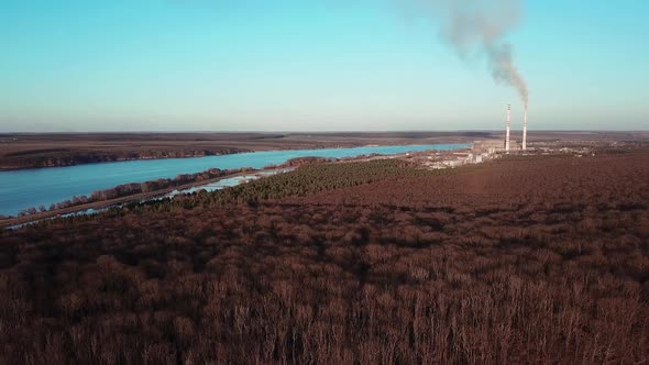 Aerial view of winter forest without snow against a background of a power station.