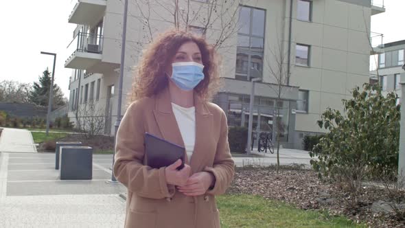 Beautiful Woman in a Protective Mask with a Tablet in Hand Walks Along a Deserted City Street