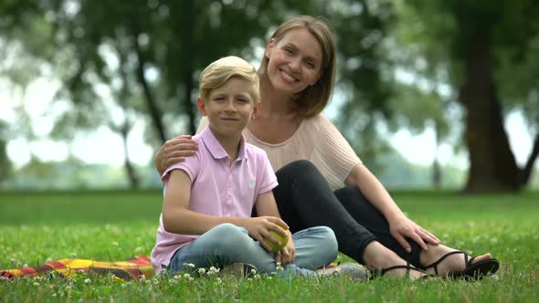 Boy Holding Apple, Sitting With Mother in Park, Concept of Healthy Nutrition