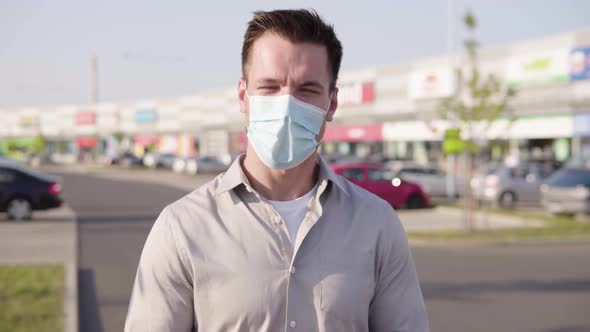 A Young Caucasian Man in a Face Mask Talks to the Camera in an Urban Area