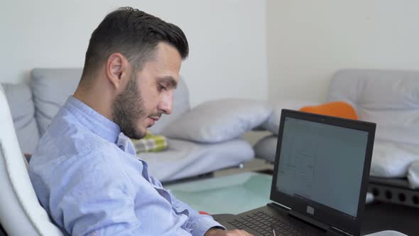 Serious Young Businessman Working on Laptop at Home Office and Taking Notes with Pen, Close Look