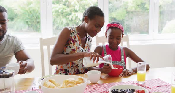 African american mother pouring milk in daughter's cereal bowl at home