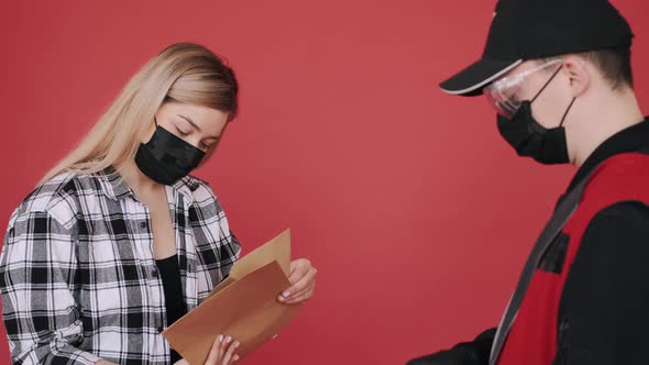 Woman in a Mask Is Receiving a Parcel of Craft Paper Envelopes From a Deliveryman