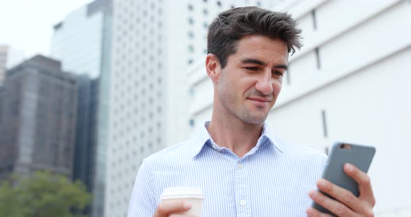 Businessman using mobile phone and holding cup of coffee