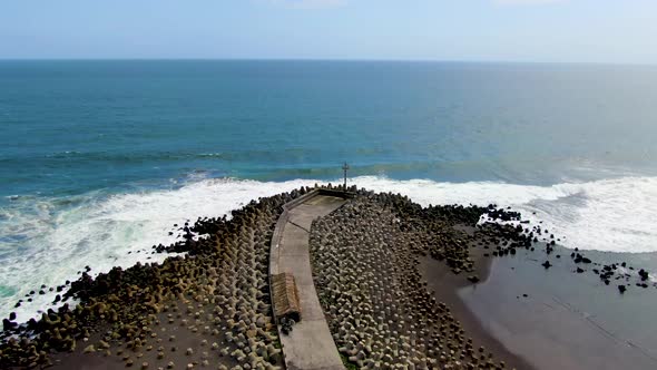 Ocean waves crashing on tetrapod breakwater, pier on Java coast aerial view