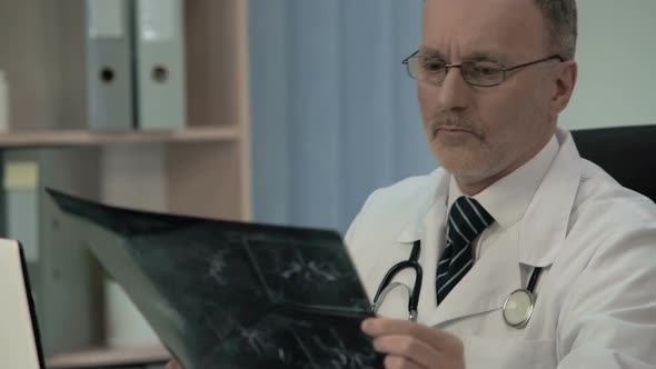 Neurologist Examining Patient Venogram and Typing His Findings in Patient Card