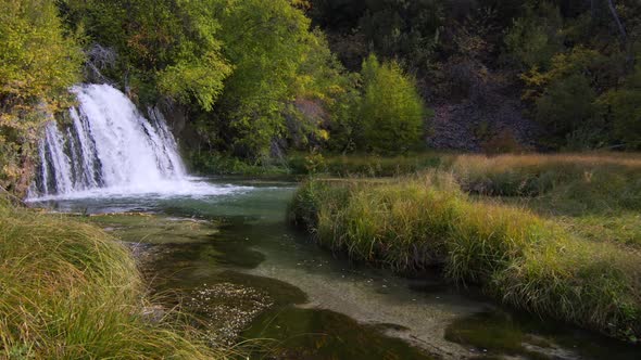 Panning view of waterfall flowing into grassy forest in Wyoming