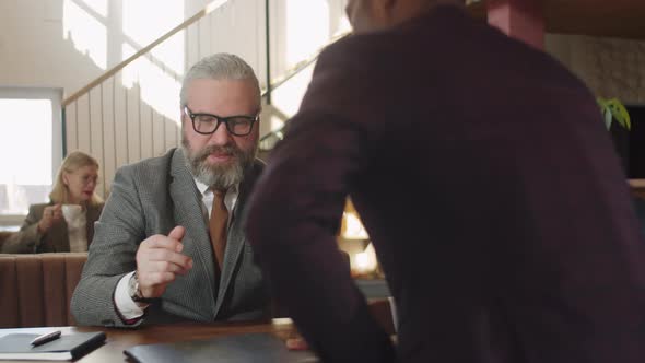 Senior Businessman Discussing Contract with Partner in Restaurant