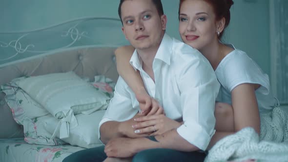 Young Beautiful Couple Sitting in the Morning on the Bed Looking Out the Window