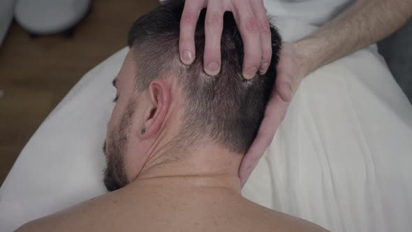 Bearded Caucasian Man Lying Face Down on Massage Bed As Masseur Massaging Head