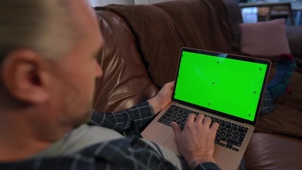 Green Screen Laptop in Hands of Man Typing Message on Keyboard Lying on Couch in Living Room