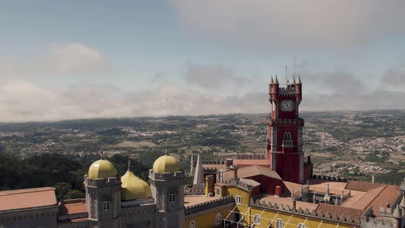 Aerial panning shot around the clock tower of Pena palace against Sintra cultural landscape.