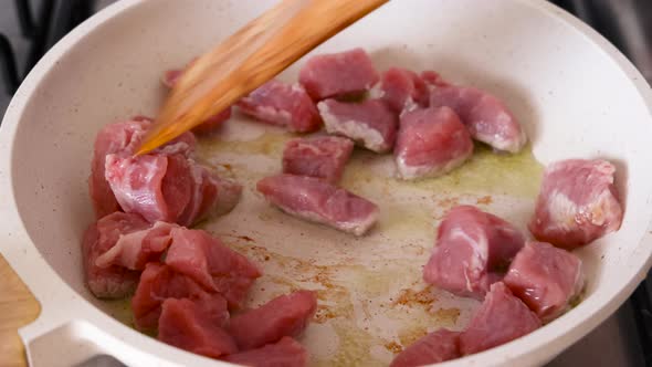Stirring pieces of raw veal meat in white frying panclose up